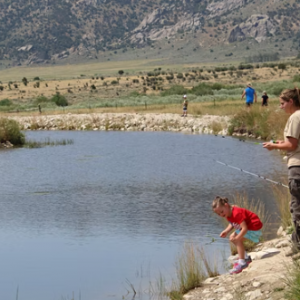 children and ranger fishing on the edge of castle rocks pond, child in red shirt is picking something up off the ground