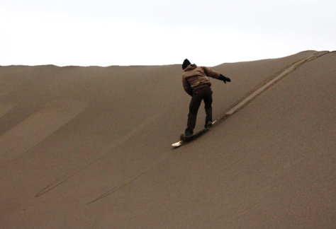 Person sandboarding down the dunes