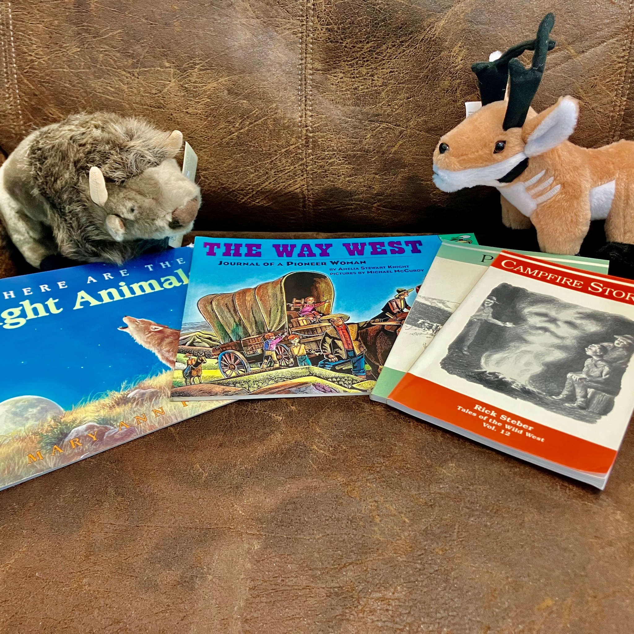 Image of two stuffed animals next to a pile of books on a couch