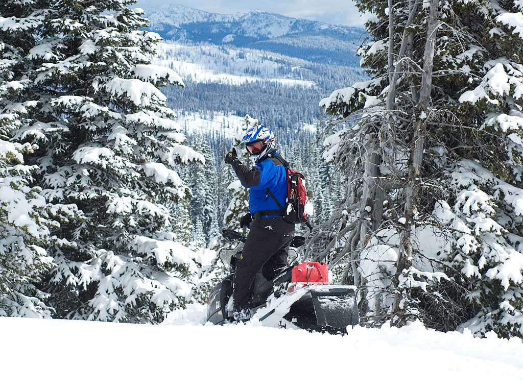 Snowmobile rider in a snowy scene with their thumb up