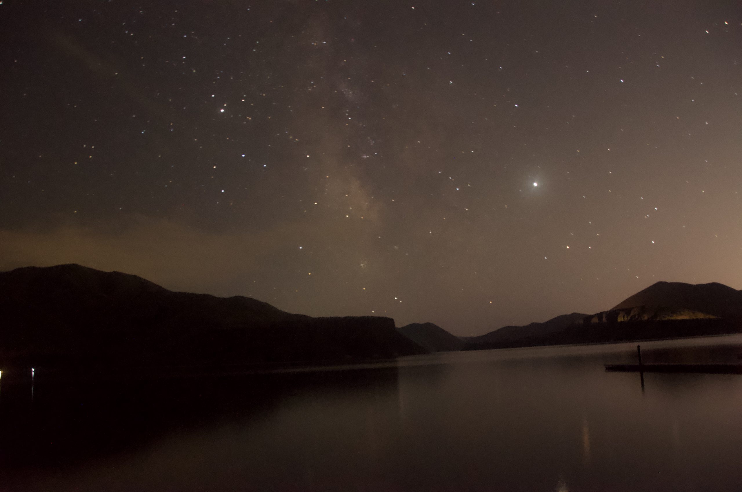 starry night sky above lake surrounded by mountain sillouettes